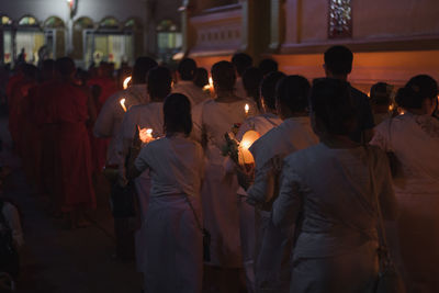 Rear view of people with lit candles walking on street during traditional festival