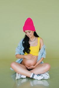 Stylish young expectant mother in stylish clothes on an olive background