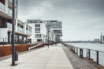 Footpath by buildings in city against sky