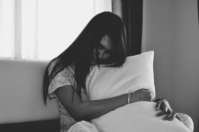 Woman embracing pillow while sitting in bedroom