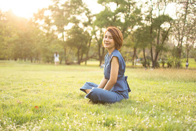 Portrait of woman sitting on field against trees