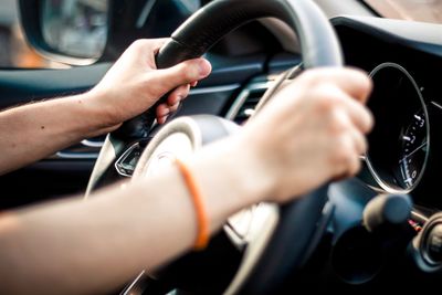 Cropped hand of man holding steering wheel in car