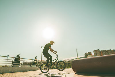 Man riding bicycle on metallic pipe against sky