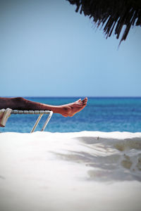 Low section of man relaxing on lounge chair at beach