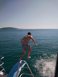 Rear view of shirtless man in sea against sky