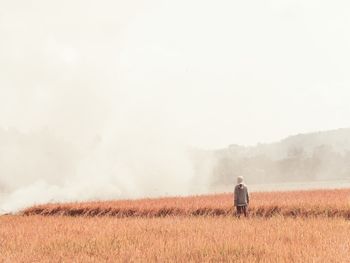 Rear view of person standing on agricultural field against smoke