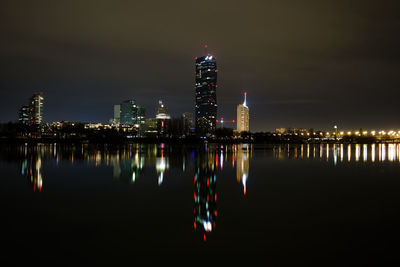 Illuminated buildings uno city in vienna  by river danube against sky at night