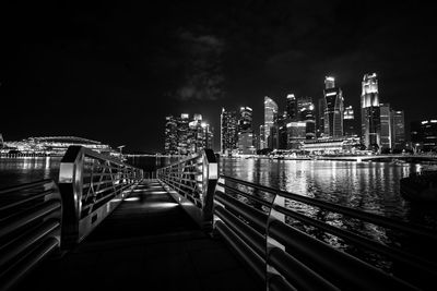 Illuminated bridge over river by buildings against sky at night