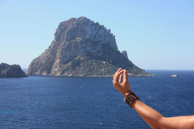 Man hand on rock by sea against clear sky