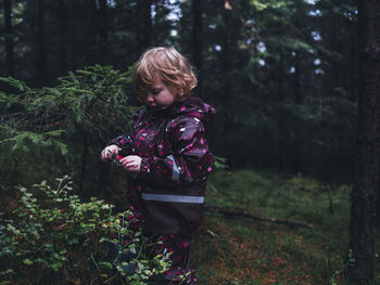 Rear view of boy standing by trees in forest