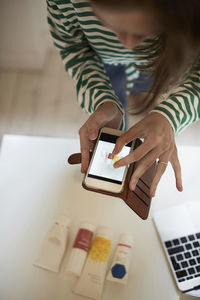 High angle view of blogger photographing beauty products with smart phone at home