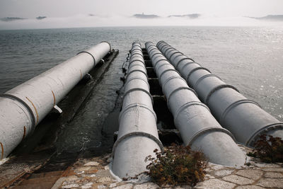 Industrial pipes over sea against sky