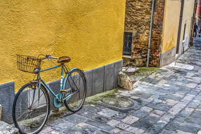 Bicycle parked on street by wall of building