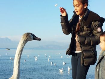 Young woman standing on swan by sea against sky