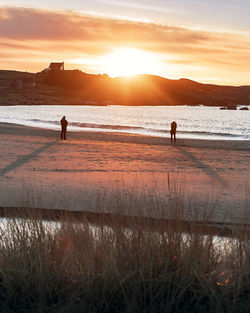 Silhouette people on beach against sky during sunset