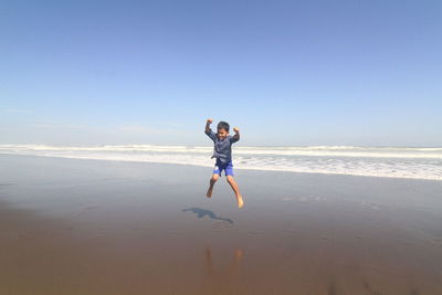 Full length of boy jumping at beach against sky