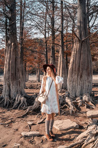 Full length of woman standing by tree trunk in forest