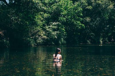 Rear view of woman swimming in lake against trees