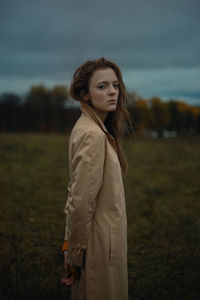 Young woman looking away while standing on field against sky