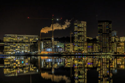 Illuminated buildings by river against sky at night