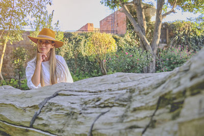 Side view of woman sitting on tree trunk