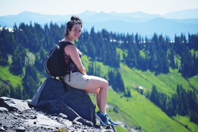 Portrait of young woman sitting on rock against mountains