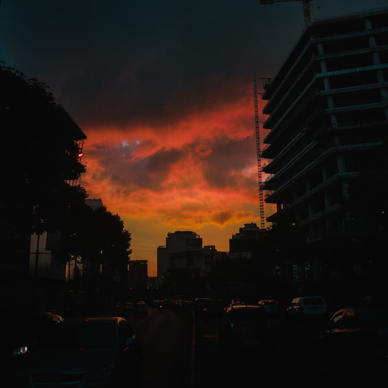 CARS ON STREET AMIDST BUILDINGS AGAINST SKY DURING SUNSET
