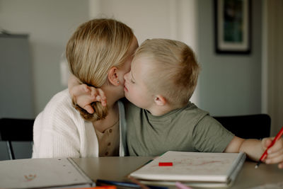 Boy with down syndrome kissing sister while sitting at dining table