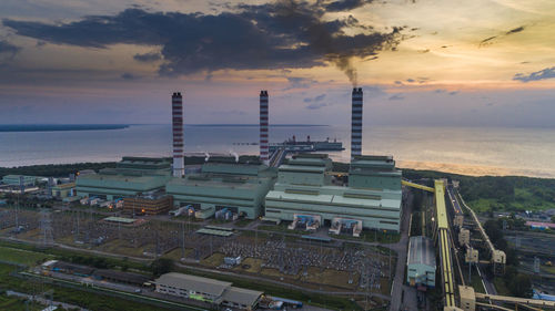 High angle view of factory by sea against sky during sunset