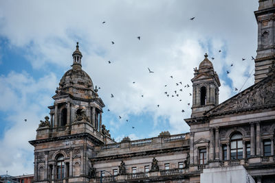 The victorian and beaux arts style city chambers of glasgow with birds flying in the sky over it