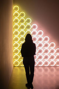 Rear view of woman standing against illuminated wall