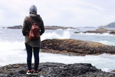 Rear view of woman standing on beach against sky