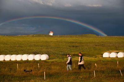 People standing on field against rainbow in sky