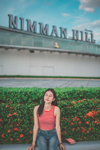 Young woman sitting by plants in city