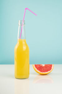 Close-up of orange drink and a grapefruit on glossy white table