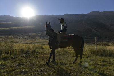 Man riding horse on field against mountains