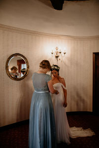 Maid of honor helping bride dress for the wedding ceremony