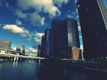 Modern buildings by river against sky in city