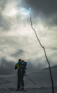 Rear view of hiker with backpack standing on snow covered field against cloudy sky during sunset