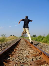 Rear view of man jumping on railroad track against sky