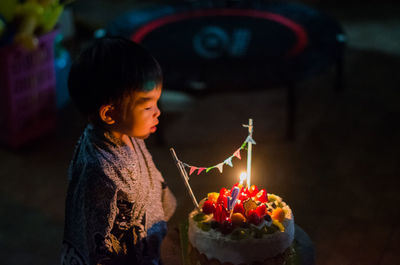 Boy looking at lit candles on cake in darkroom