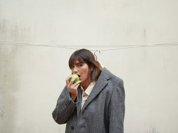 Portrait of a beautiful young woman drinking water against wall
