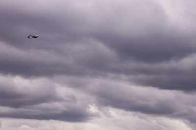 Low angle view of airplane flying against cloudy sky