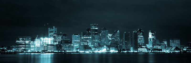 Illuminated buildings by sea against sky at night
