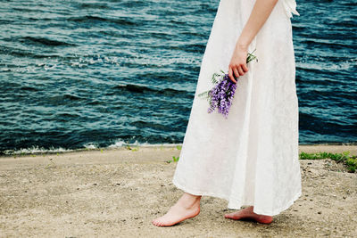 Low section of woman holding lavenders on shore