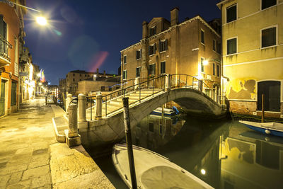 Arch bridge over canal amidst buildings in city at dusk