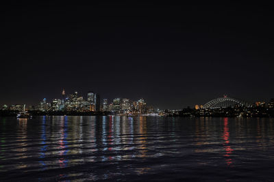 Illuminated city by sea against sky at night