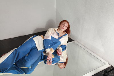 Fashion portrait of ginger woman in fashionable stylish summer suit sitting on mirror, studio