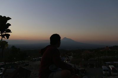 Silhouette man standing by cityscape against sky during sunset