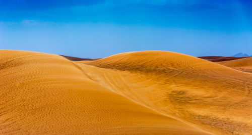 View of sand dunes in desert against blue sky